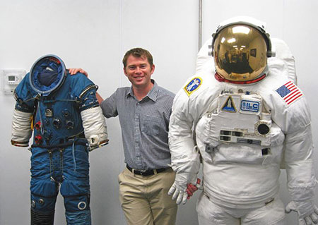 James Waldie poses with NASA Extravehicular Activity suits used for spacewalking.