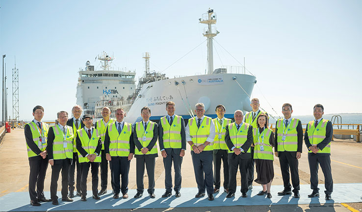 A group of people in high visibility vests stand in front of a ship docked at port