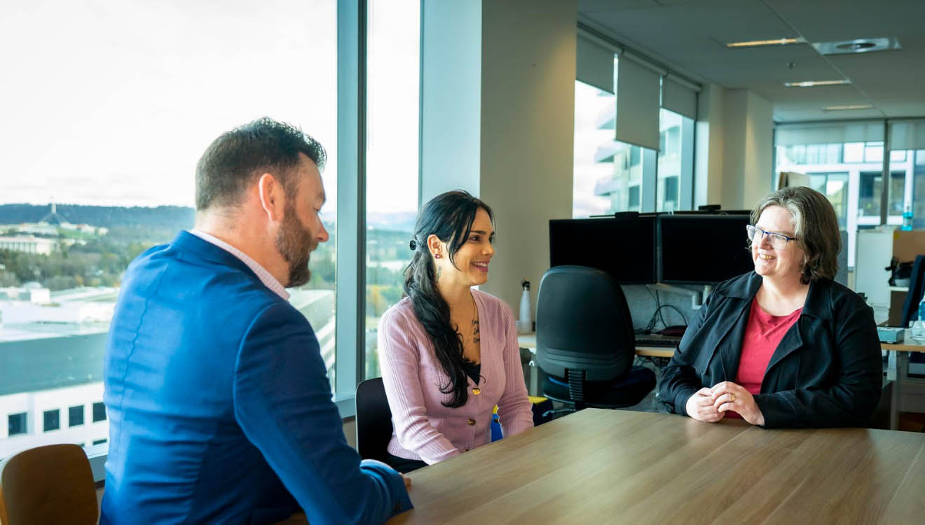 Image depicting our inclusiveness at the department as three employees sit around a table discussing a matter together openly. 