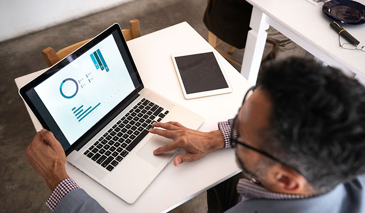 A man working on a laptop. The laptop screen has charts on it.