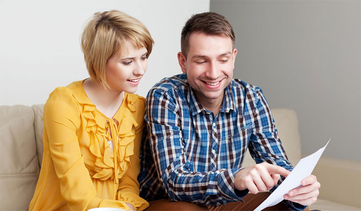 A young couple, woman on the left and man on the right, are looking at an energy bill together and smiling.