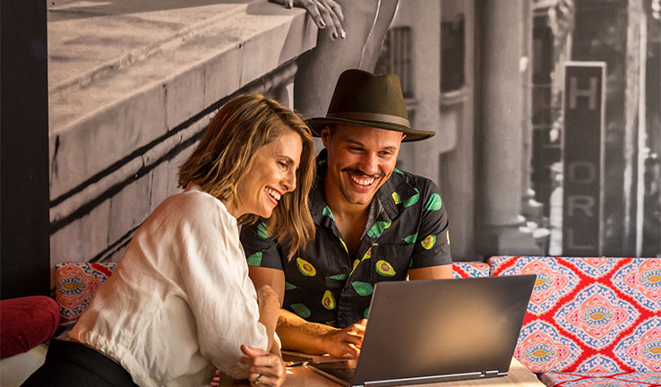Photo showing an Indigenous entrepreneur, and a female entrepreneur, looking at a laptop in an informal office environment.