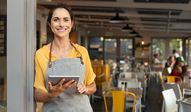 Photo of  a woman holding an ipad, with a restaurant behind her
