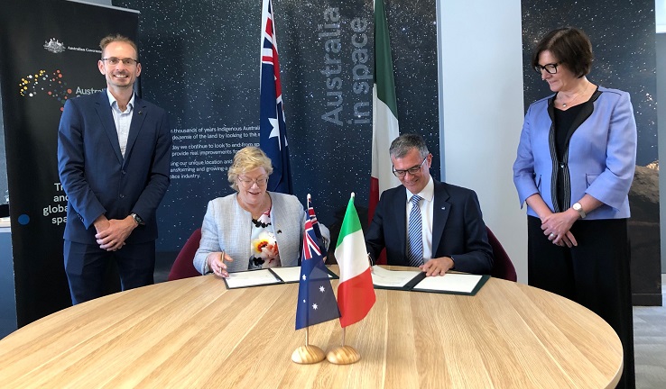 Four people at a table, the middle two seated. Australian and Italian flags on the table.