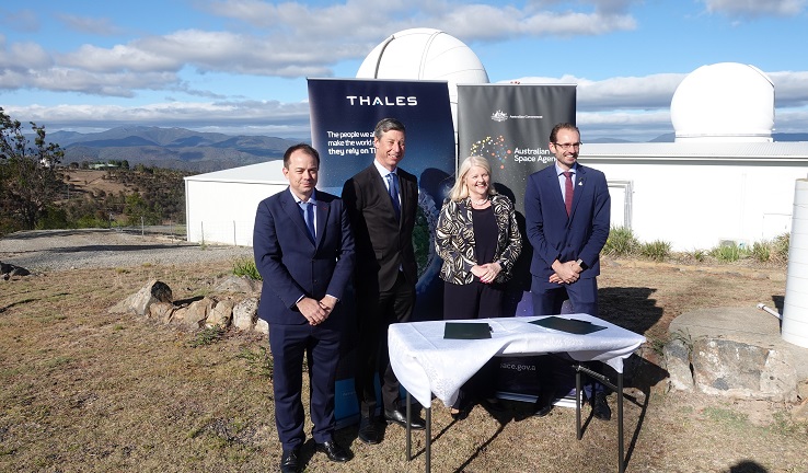 Four people standing behind a table, with a space telescope behind them