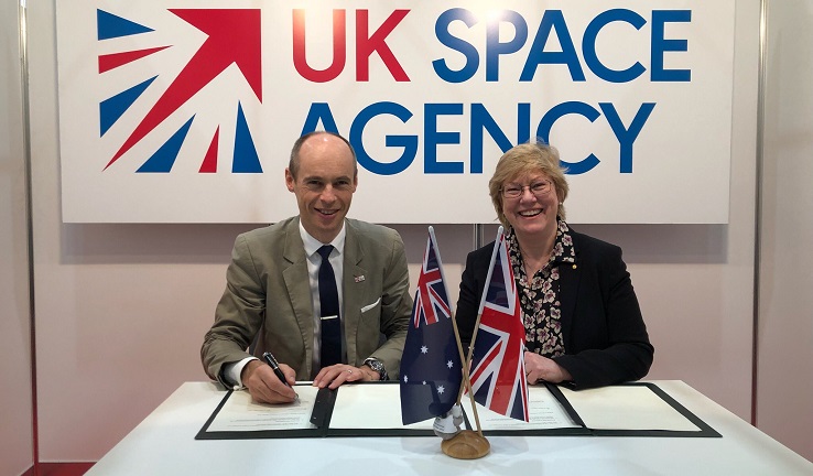 A man and a woman sitting at a table with a UK Space Agency sign behind them and Australian and British flags on the table.