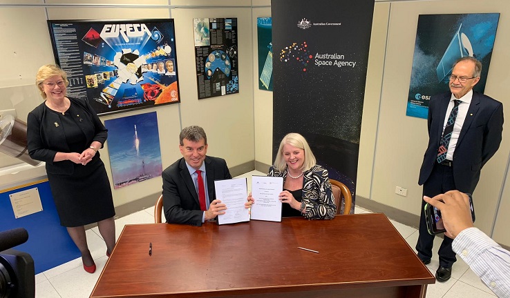 Two people holding up documents and sitting at a table, with two people standing behind them