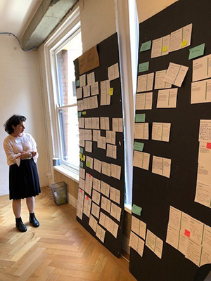 A woman in front of a board. Many pieces of paper with ideas written on them are pinned on the board.