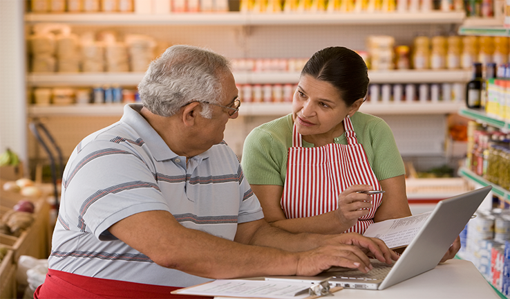 Two people sitting in a shop looking at a laptop.