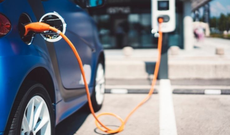 Image of an electric vehicle in a parking lot, plugged into a charging station.