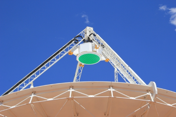 A green circular Phased Array Feed receiver, housed in white casing designed by Innovation Composites, sits on top of an ASKAP telescope dish pointing to the sky