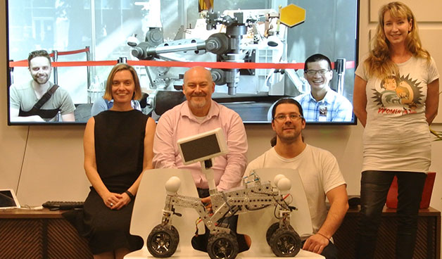 Four people from the Akin team are pictured in Australia, in front of a web monitor. On the web monitor are two people from the Akin team who are located in USA, with an Akin AI crew robot.