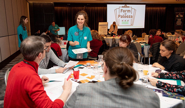 : A group of people sit around a table, talking to a facilitator from PM&C’s BETA team.