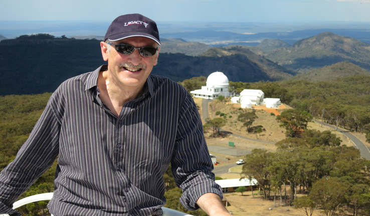 Astronomer-at-large, Fred Watson, with the Siding Spring Observatory at a distance in the background. Astronomer-at-large, Fred Watson, poses for a photo with the Siding Spring Observatory at a distance in the background.