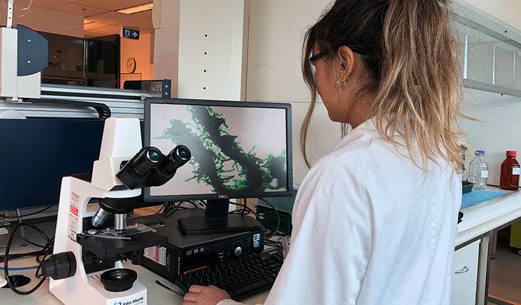 A woman in a laboratory coat looking at a computer and microscope.