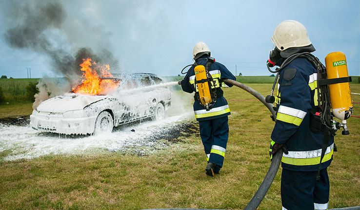 Two firemen wearing breathing apparatus, extinguishing a car fire