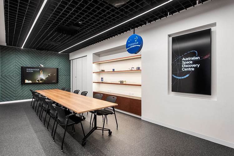 A meeting room with a large desk and 12 chairs around it. There is a screen at the end of the table that says 'Endeavour room'.