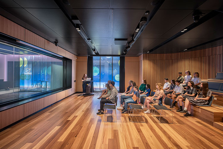 People sitting in chairs facing a window looking out on to the control centre.