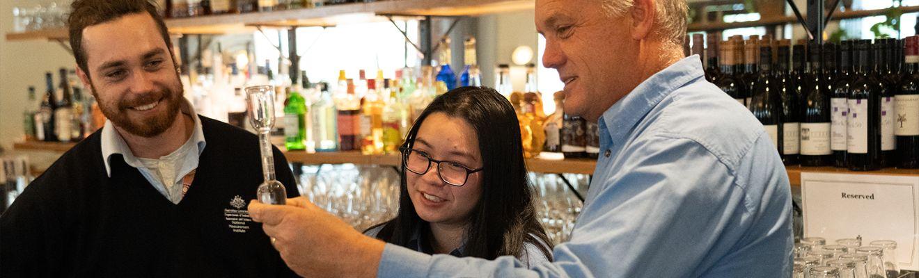 Three people stand in a bar measuring a drink