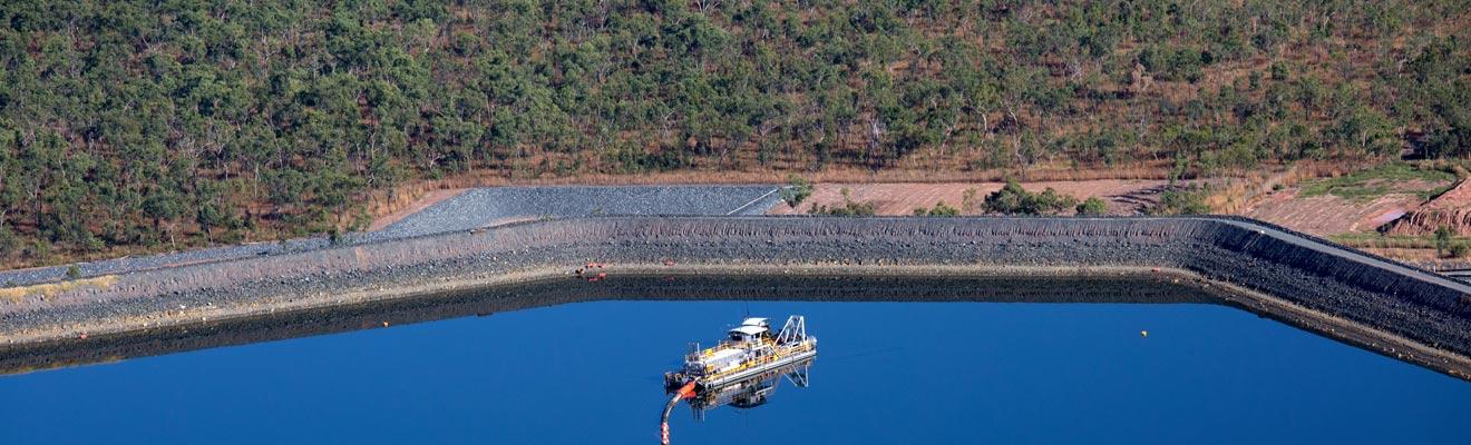 Aerial photo of a boat in a large pond, with northern Australian bushland in the background 