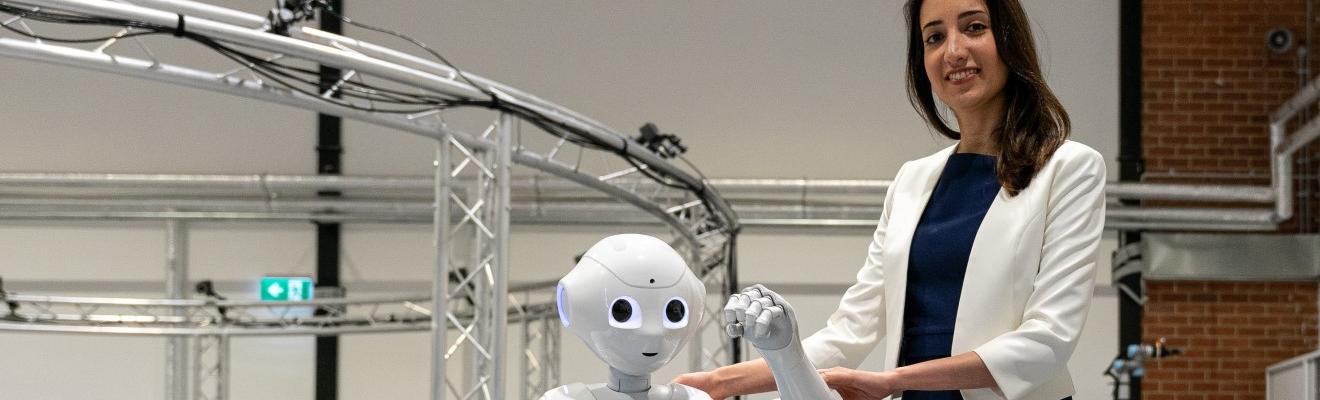 Elahe Abdi standing next to a robot.