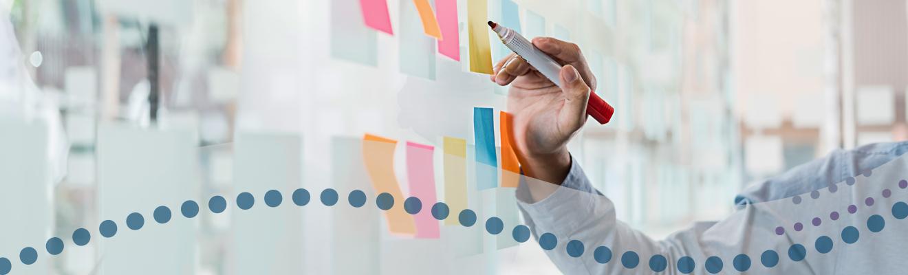 Close up of hand holding pen and sticky notes on wall