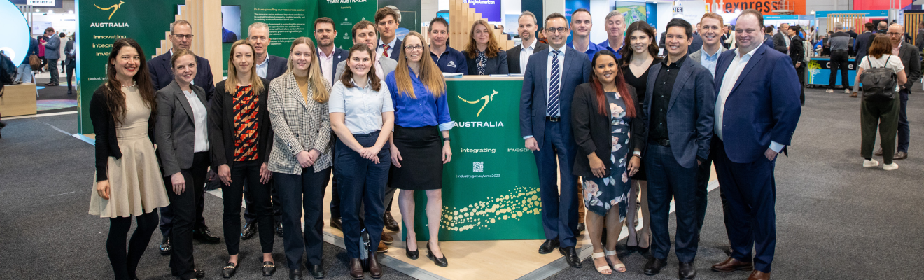 A group of people in business attire standing at a large, open plan exhibition stand at the 2023 World Mining Congress. The stand displays the Australian Government’s green and gold ‘Nation Brand’, including a kangaroo and decorative elements representing Australia’s rivers and bush tracks.