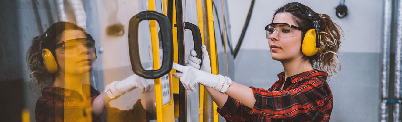 A young woman wearing safety goggles and ear protection operating machinery in a factory