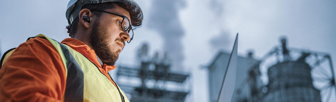 Man wearing protective gear standing in front of oil and gas infrastructure.