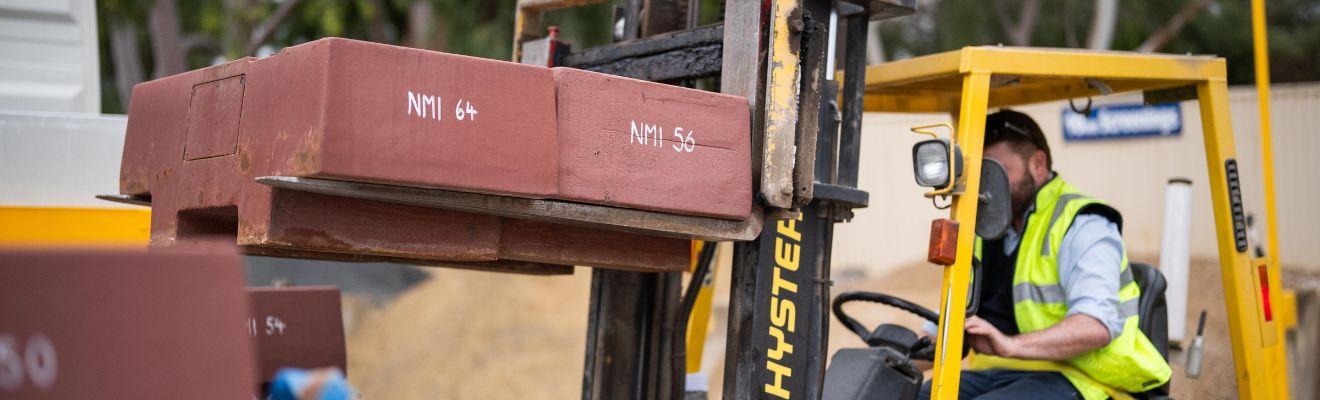 Photo of a man driving a forklift that is carrying weights.