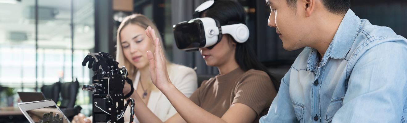 Woman using a VR headset and robotic hand while 2 other people watch