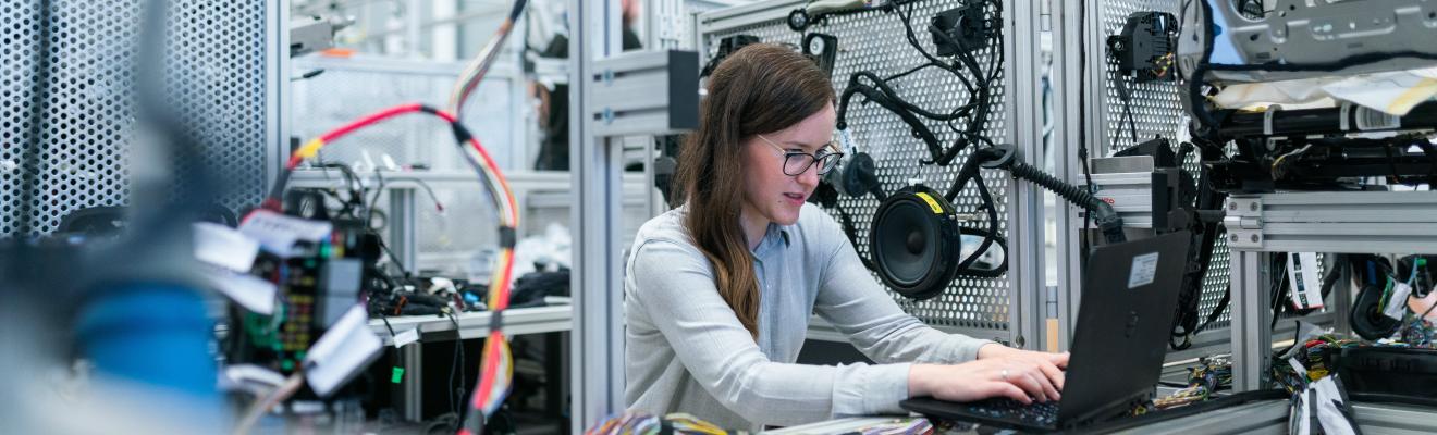 A woman working at a computer in a robotics workshop. 