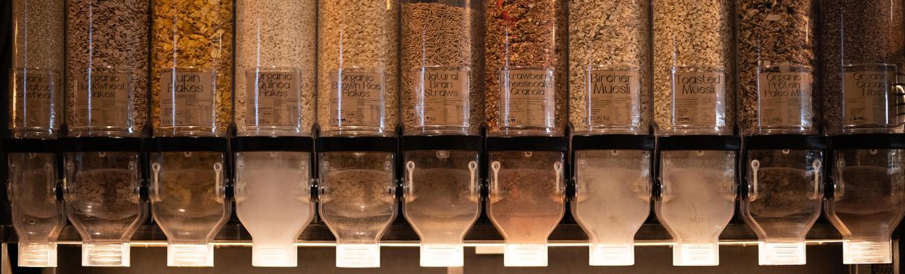 Vertical plastic dispensers at a wholefoods shop, filled with various types of cereals