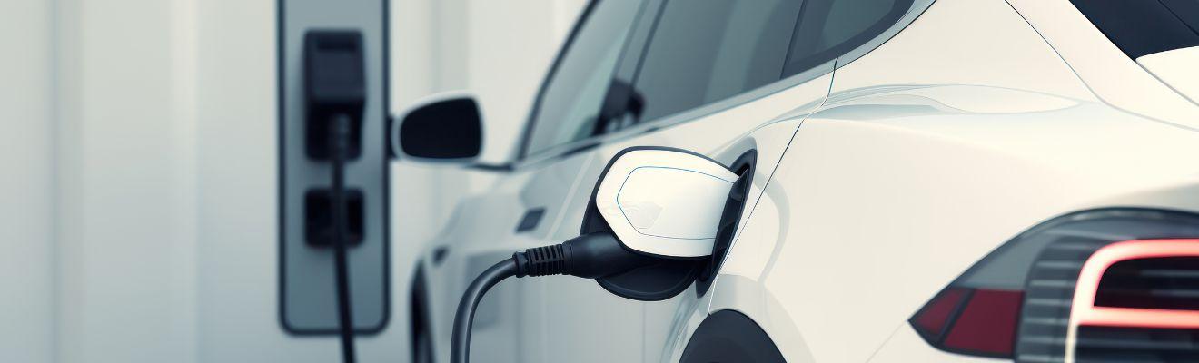 Photo of the back end of a white electric vehicle with a charging cable plugged in. The electric vehicle supply equipment (EVSE) is in the background.