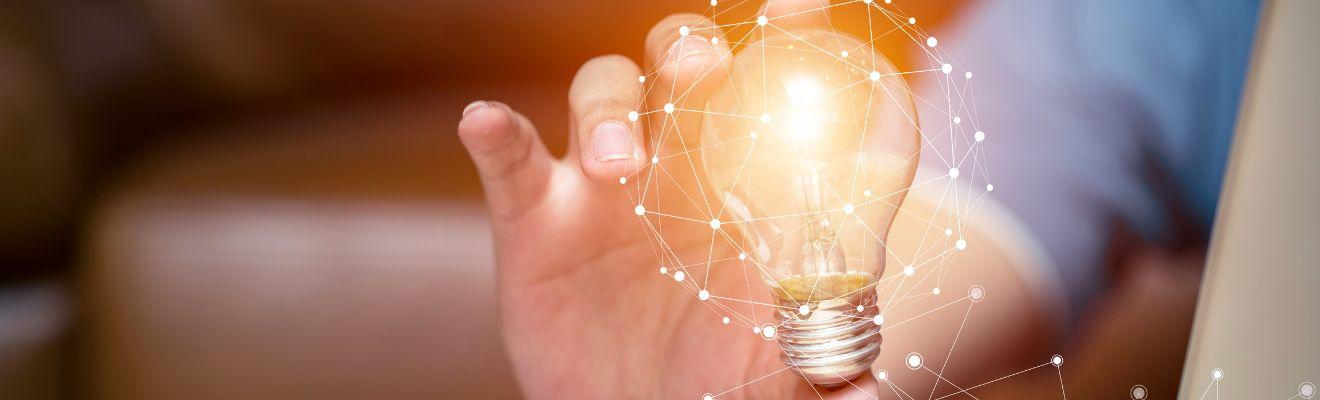 Close up of a hand holding a light bulb with an abstract network overlay 