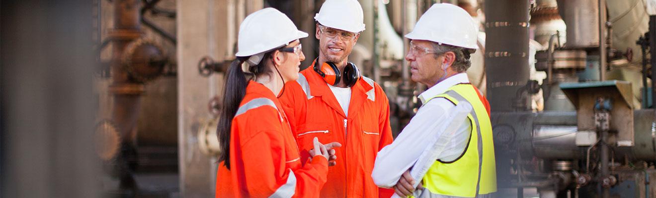 Three people wearing protective clothing meet on an offshore oil and gas facility