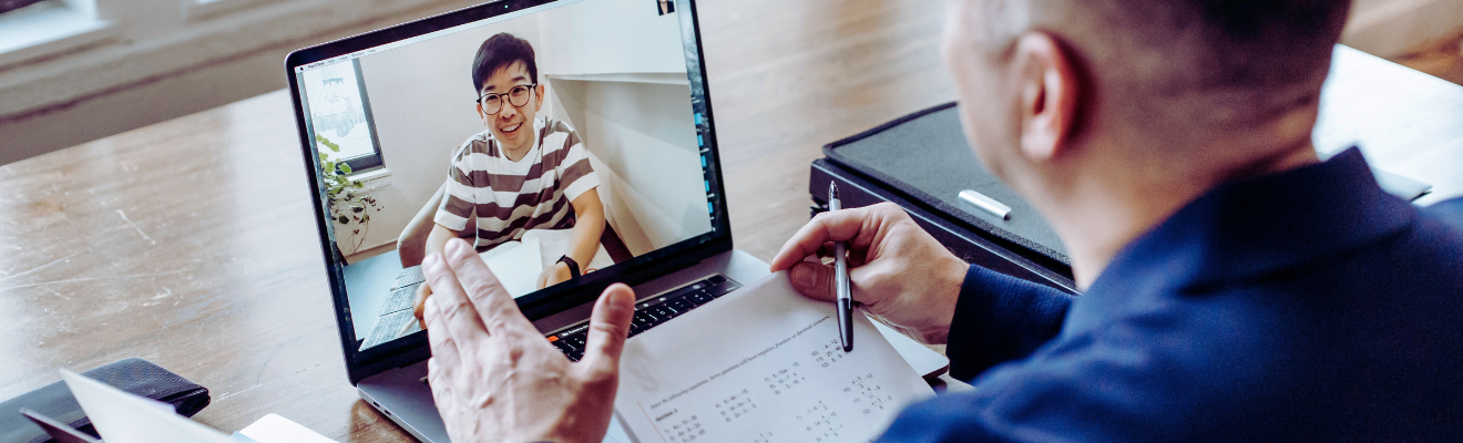 Man at desk talks to another man via video conferencing