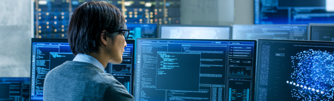 Person sitting at a desk with three computer monitors in front of them displaying artificial intelligence-related data. 