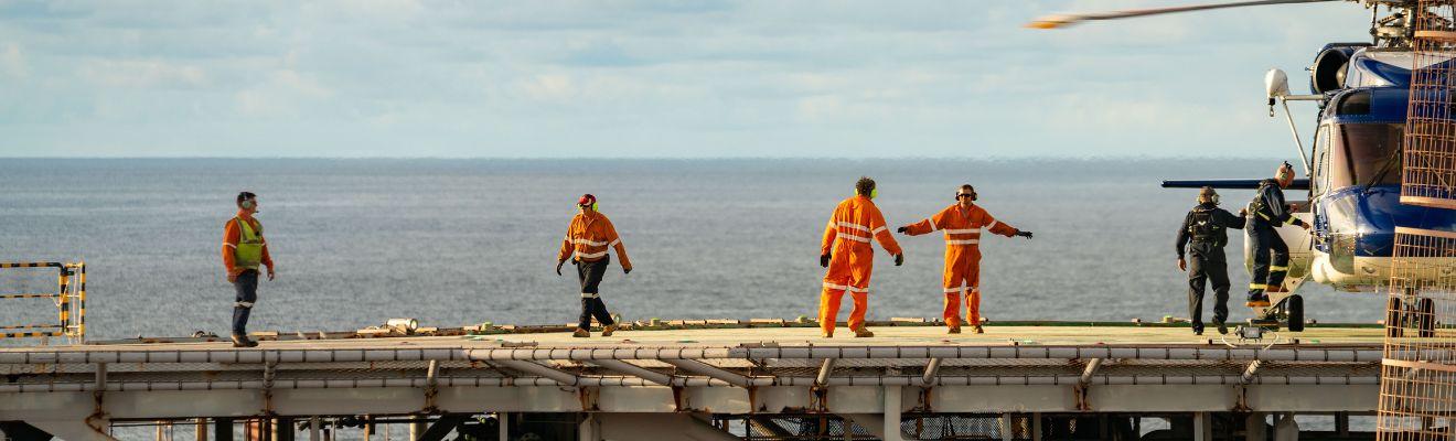 Crew members board and monitor a helicopter on a helideck offshore.