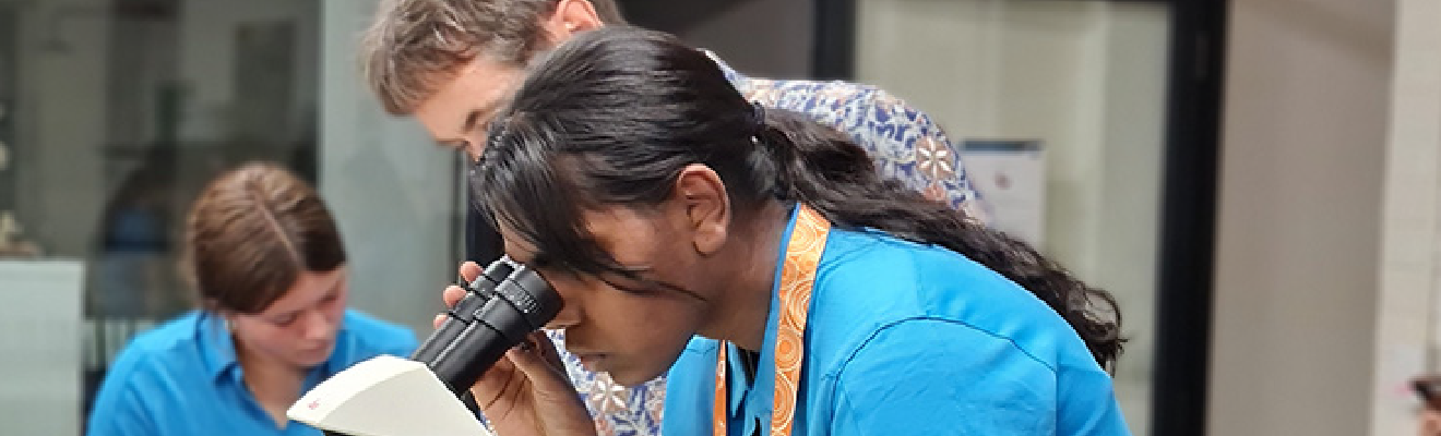 Female student looking into a microscope while a teacher looks on.