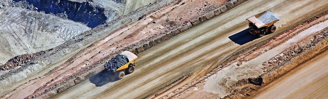 Two mining trucks drive along a road.
