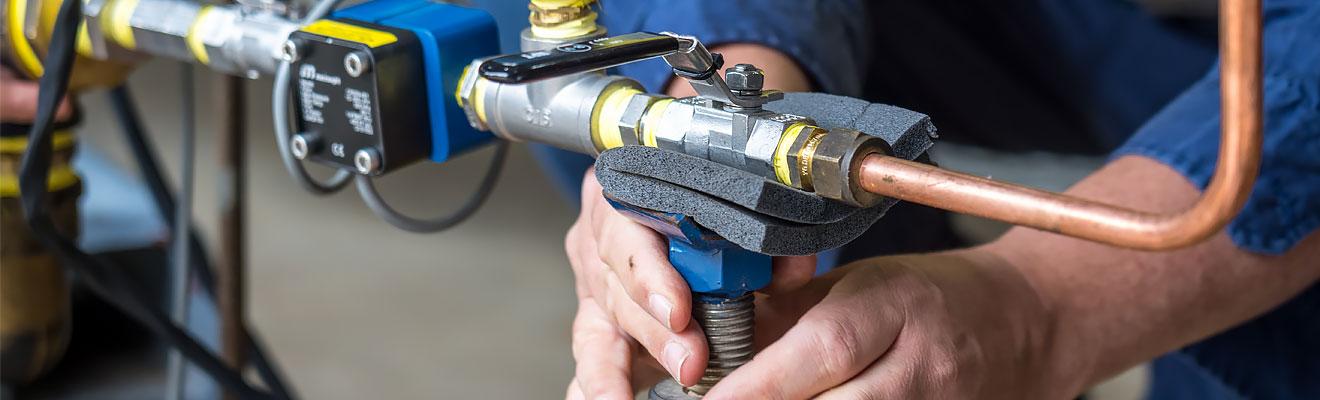 A person in high-visibility workwear adjusts the meter attached to some copper piping