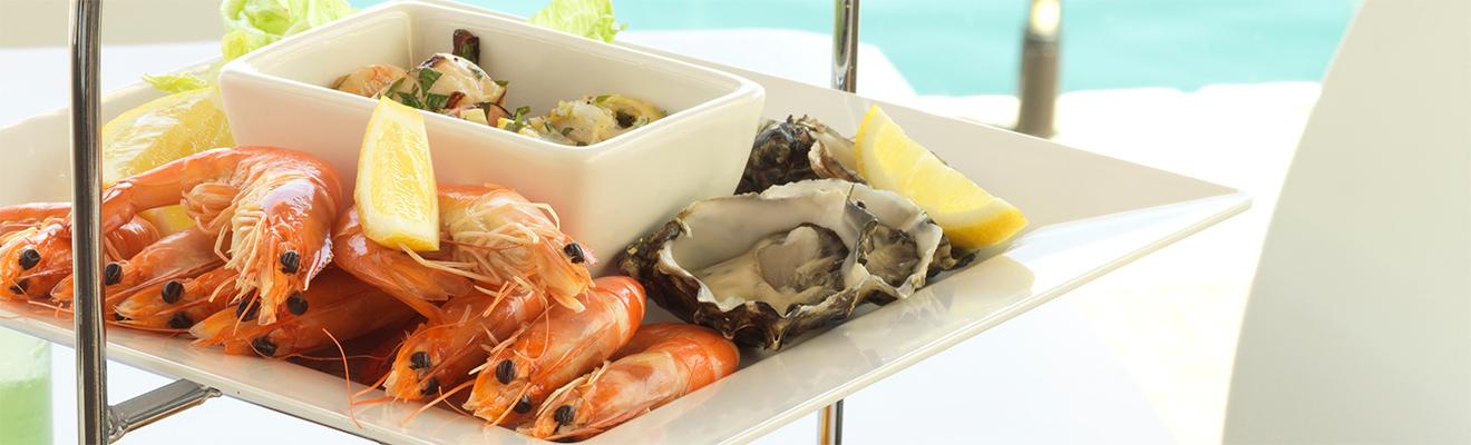Cooked prawns and fresh oysters arranged on a white platter, served with lemon wedges.