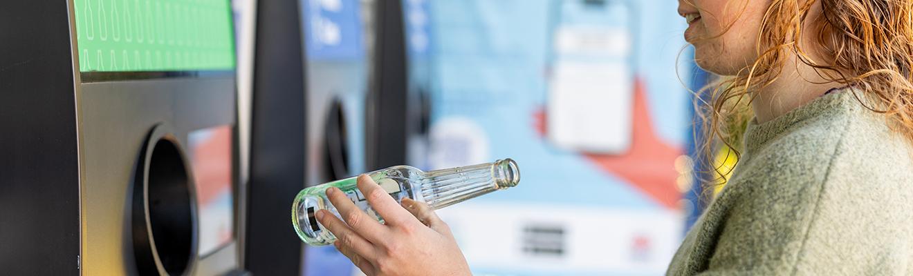 Young woman using a bottle recycling machine. 