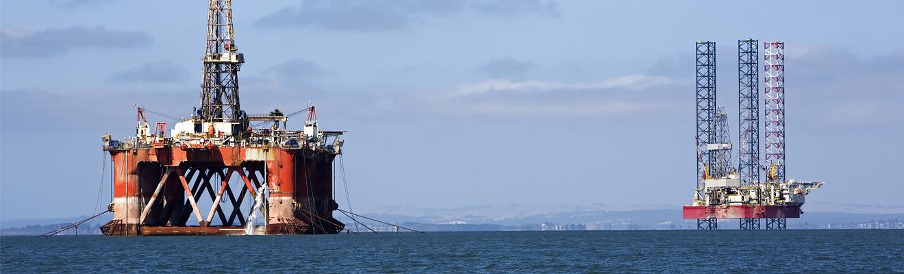 Two large mobile offshore drilling units sit in a calm blue ocean in the daytime