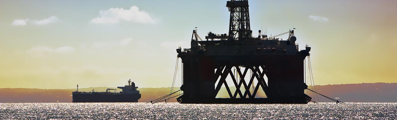 Silhouette of a mobile offshore drilling unit with a support vessel alongside in a calm ocean at sunset