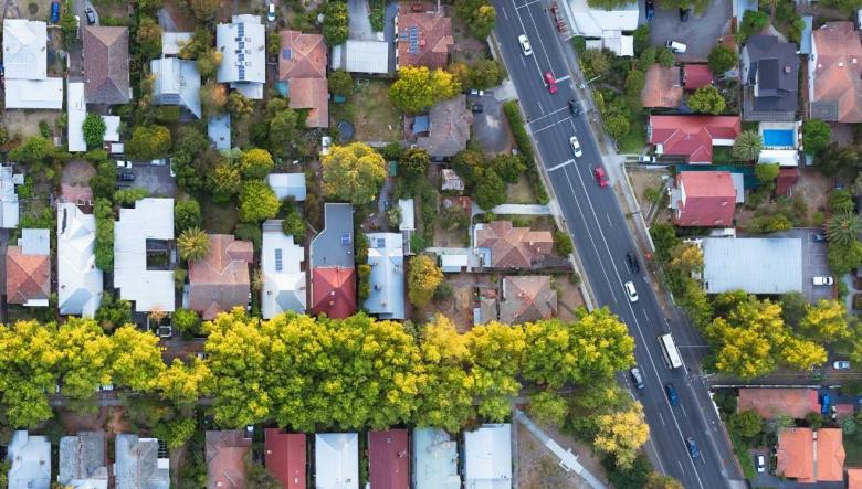 Aerial shot of houses and cars driving on a road through a suburb.