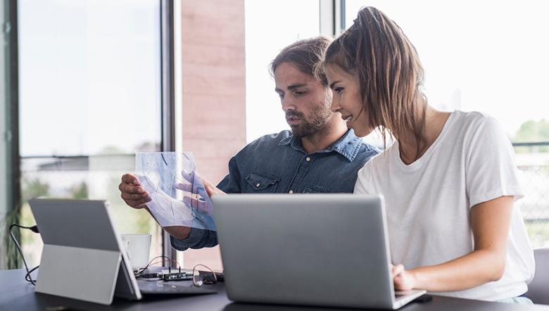 Woman and man seated at laptop computers and looking at a blueprint