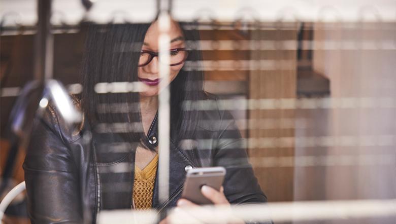 A young woman looking at her phone. We see her through the window of a café