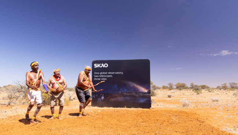 3 men in Wajarri cultural clothing dance on red dirt